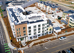 Aerial photo of a four-story apartment building with brown and white walls and solar panels on the roof.